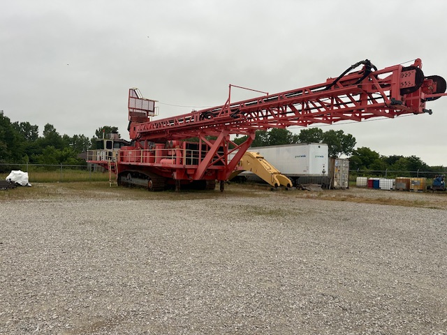 Side view of a red Sandvik D90KS rotary blast hole drill with its drill mast lowered horizontally.