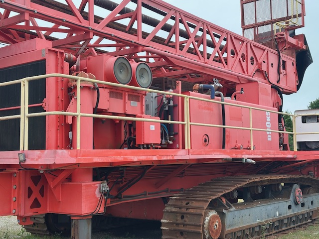 Rear-side view of a red Sandvik D90KS rotary blast hole drill, showing the access platform, machinery components and tracked undercarriage.