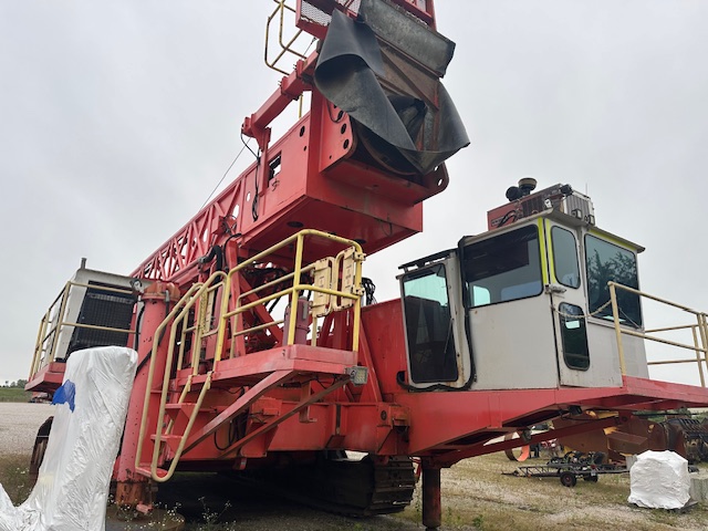Side view of a red Sandvik D90KS rotary blast hole drill with operator cabin and raised drill mast.