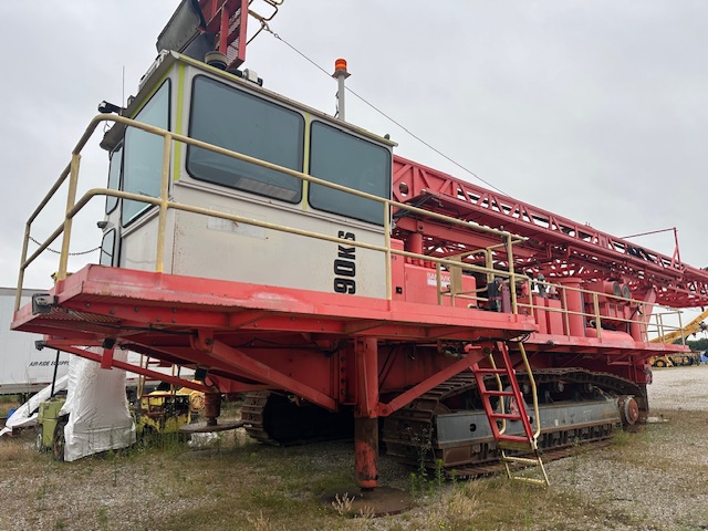 Front-side view of a red Sandvik D90KS rotary blast hole drill with operator cabin, access platform and tracked undercarriage.