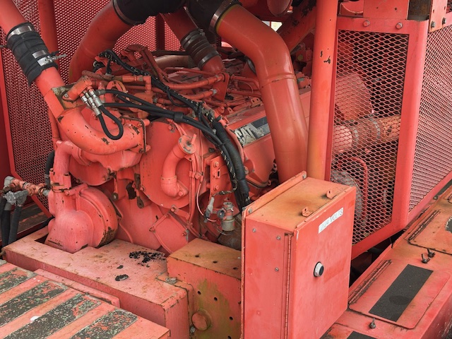 Close-up of the engine and hydraulic components of a red Sandvik mining machine.
