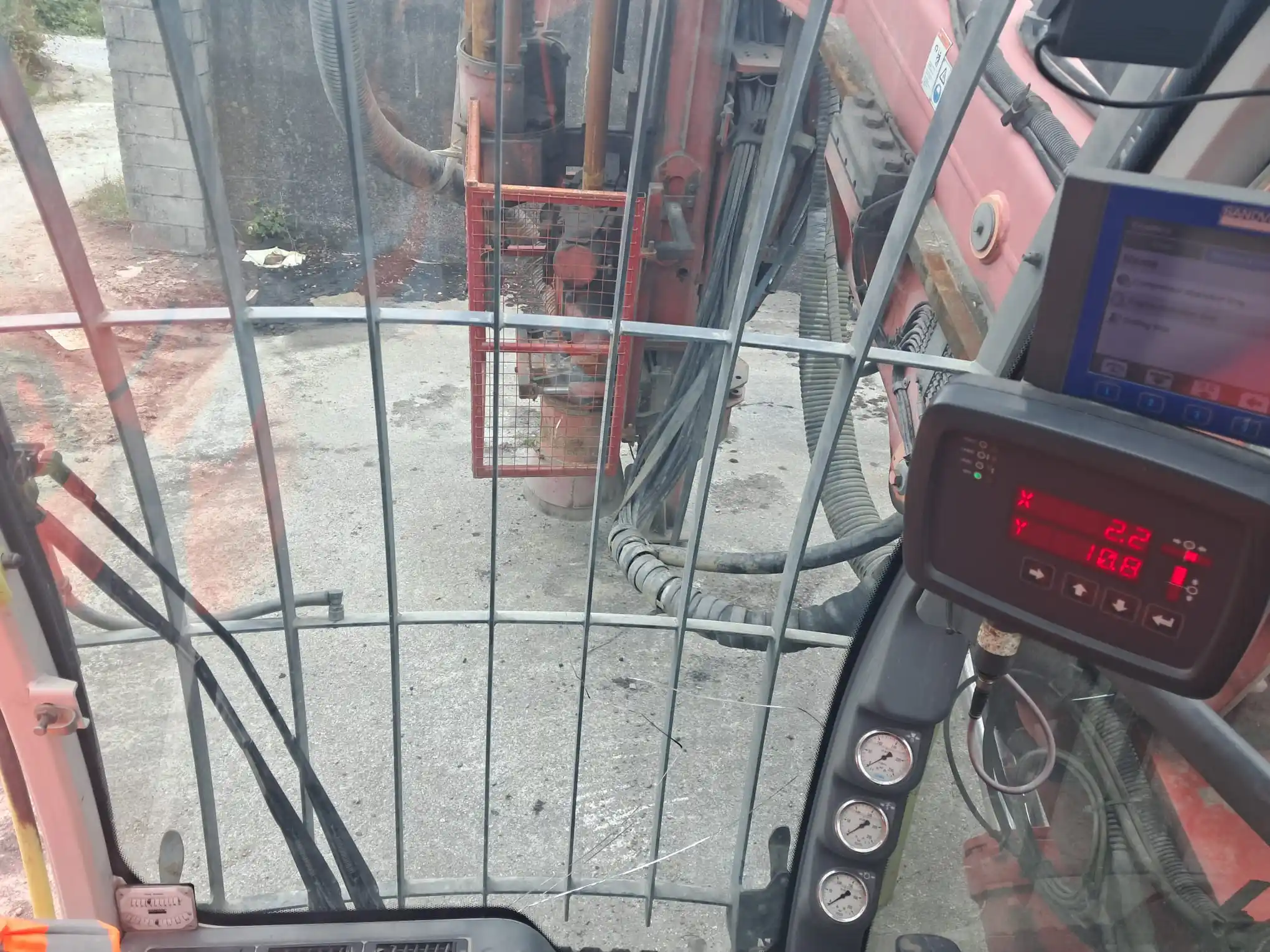 View from inside a drill rig cabin showing the control panel, safety grille and drilling equipment.