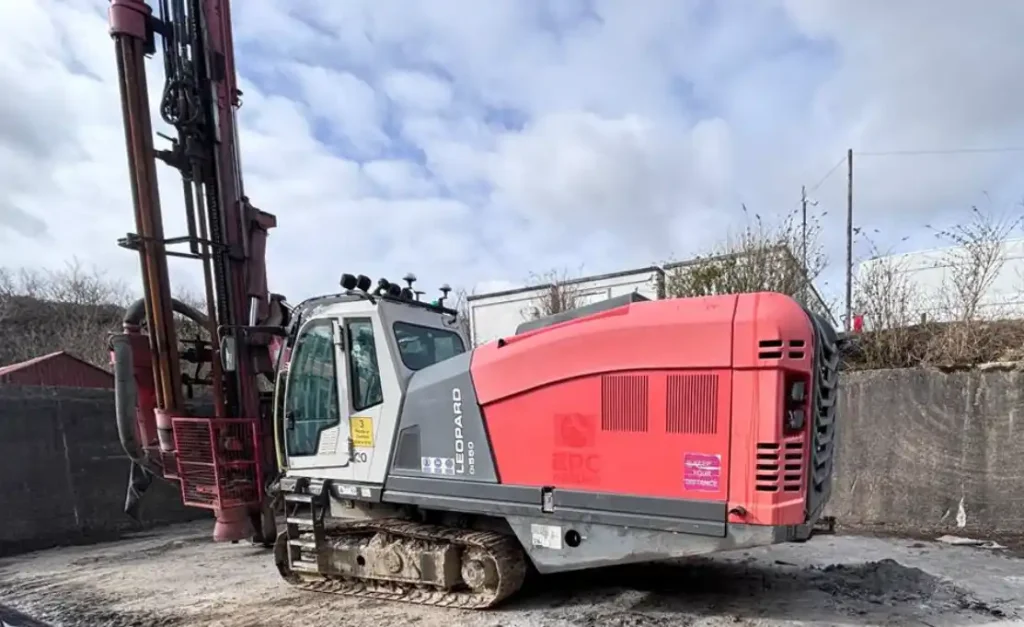 Red and grey Sandvik Leopard crawler drill rig with a raised drilling mast.